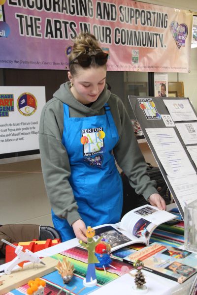 Flipping through pages, junior Lily Underwood helps the Fenton Arts Council booth. On March 1, the Fenton Expo took place at the high school.