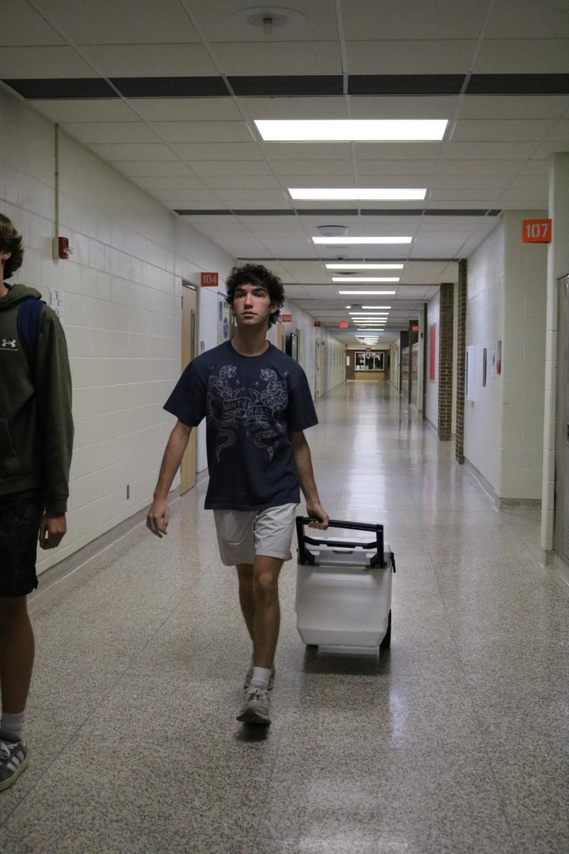 Walking, senior Owen Baize carrys a cooler through the hallway. On Sept. 17, students participated in the homecoming spirit day, anything but a backpack.
