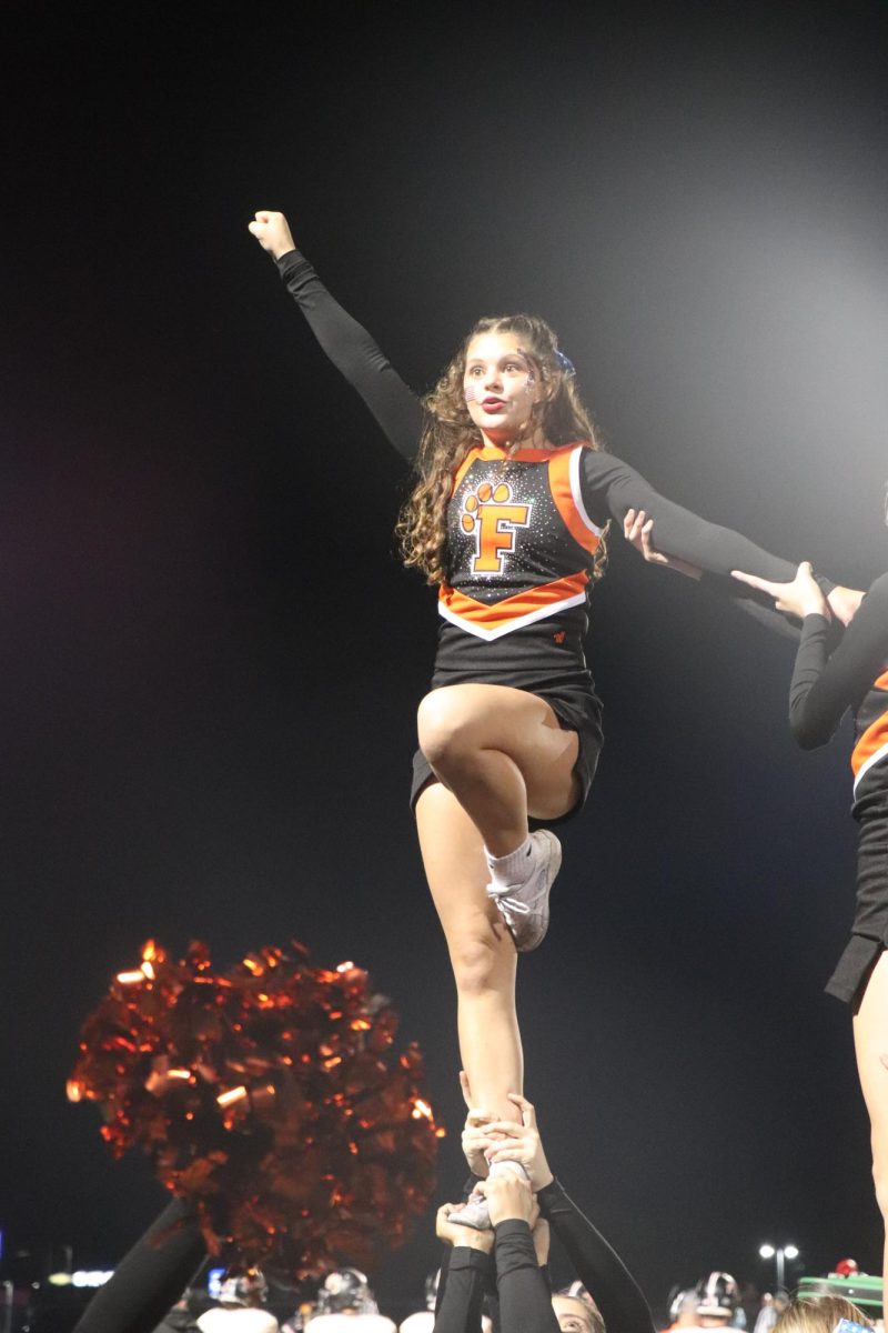 Flying in the air, junior Kenna Bigger gets ready to cheer to the crowd. On Sept. 12, the varsity cheer team performed during the varsity football game on the sideline. 