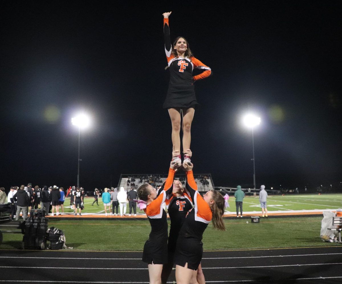 Waving at the top of her stunt, Freshman Genevieve Kilpatrick cheers at the JV game. On Oct. 16, JV cheer performs on the sideline of the Fenton vs. Goodrich game and executes one of their newest stunts. 