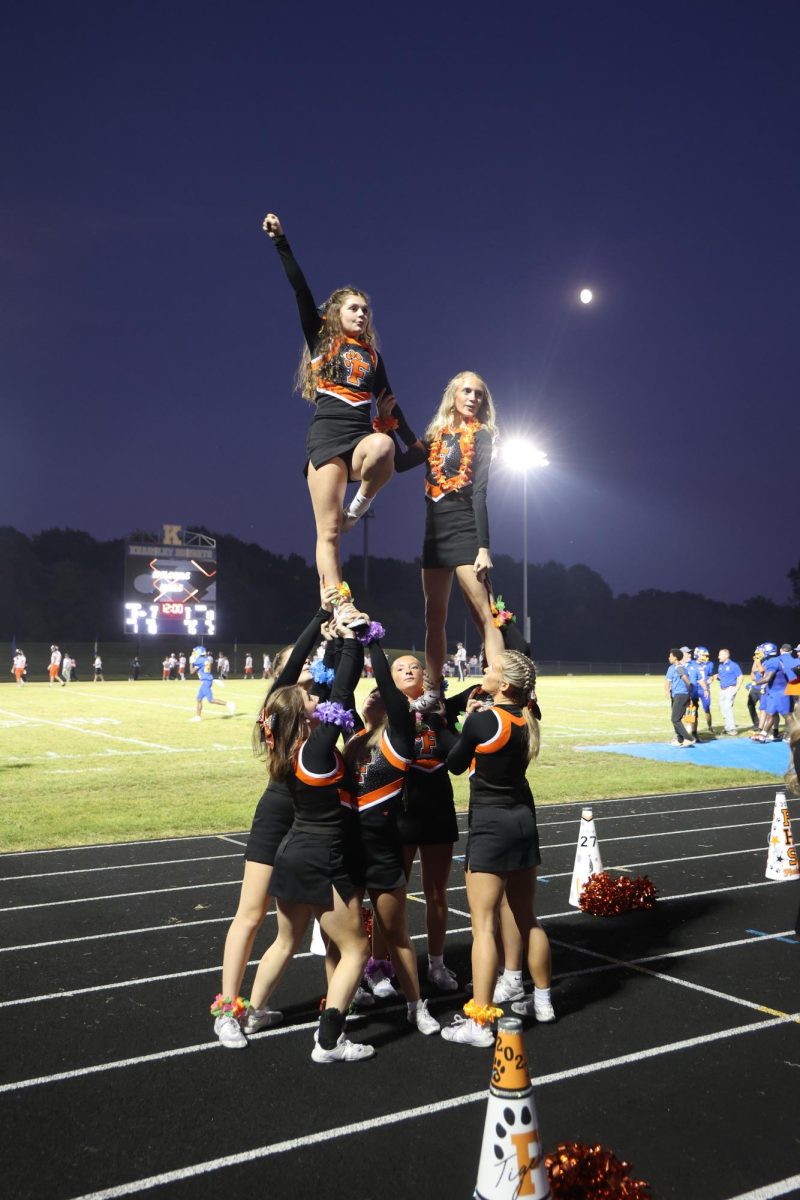 Soaring through the air, junior Kenna Bigger and team perform a stunt. On Oct. 3, the varsity cheer team cheered on the sidelines during the varsity football game. 