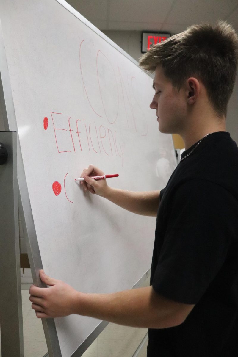 Writing on a whiteboard, junior Spencer Phipps participates in making a video. On Oct. 29, International Baccalaureate Chemistry and Biology worked on a project for current world issues.
