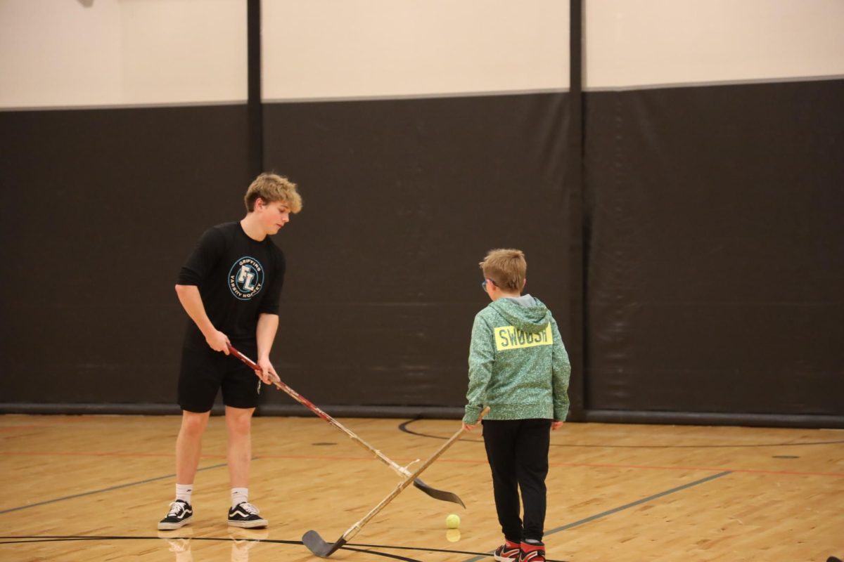 Hitting the ball, Senior Keagan Myers is helping play hockey with the kids at the hockey lock-in. On Nov. 21, Fenton and Linden hockey team helped out at the hockey lock-in.