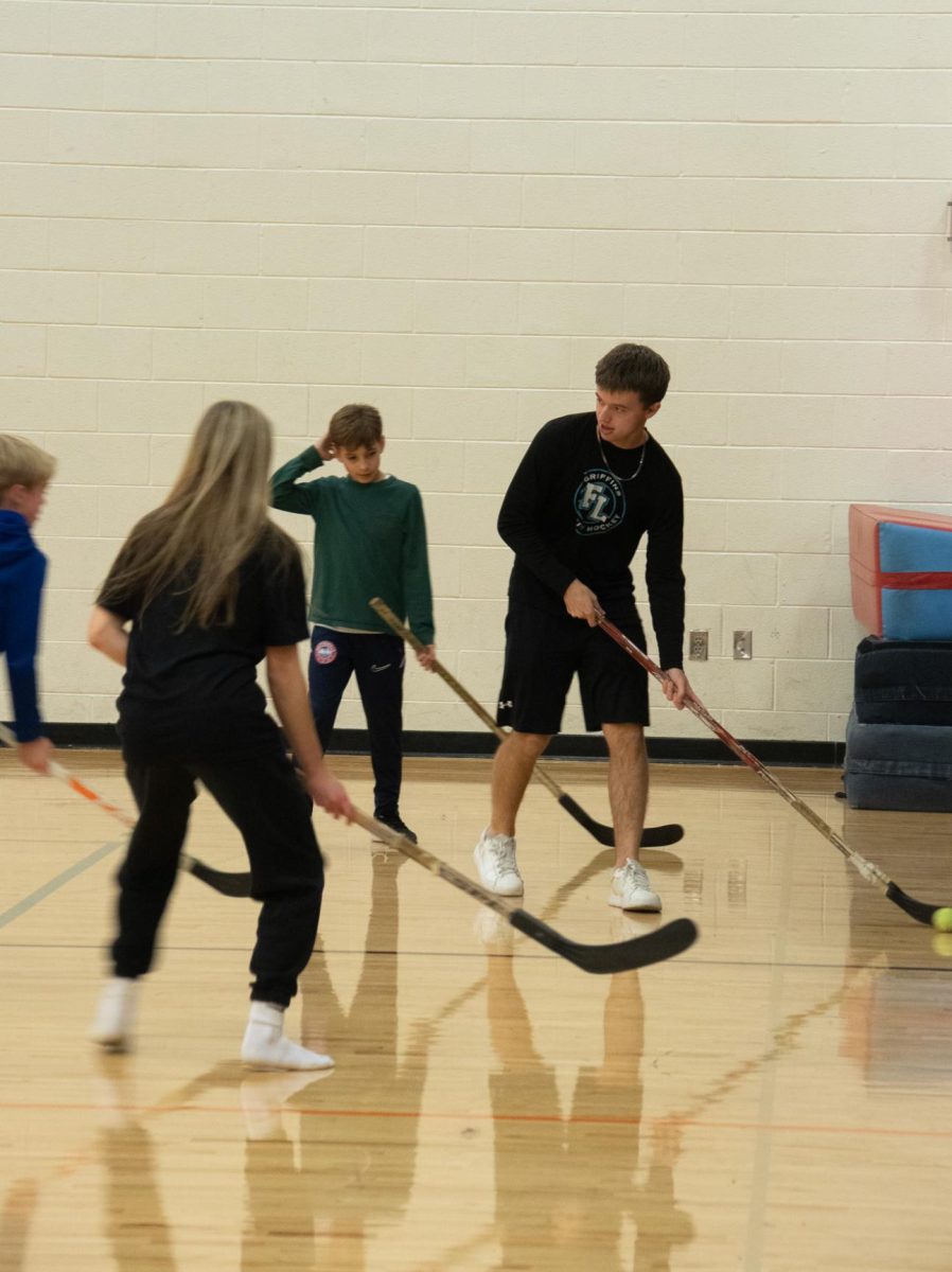 Hitting the ball, Senior Mason Wright plays hockey with the kids. On Nov. 21,the boys varsity hockey team volunteered at the hockey lock-in.