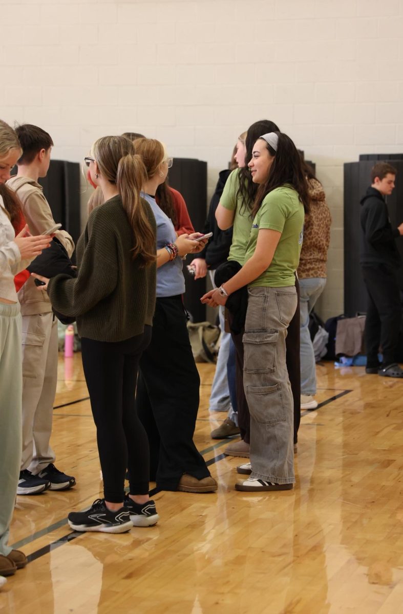 Talking to a classmate, junior Janessa Bemman lines up for ECO club photos. On Jan. 8, club photos were taken in the Auxiliary gym.
