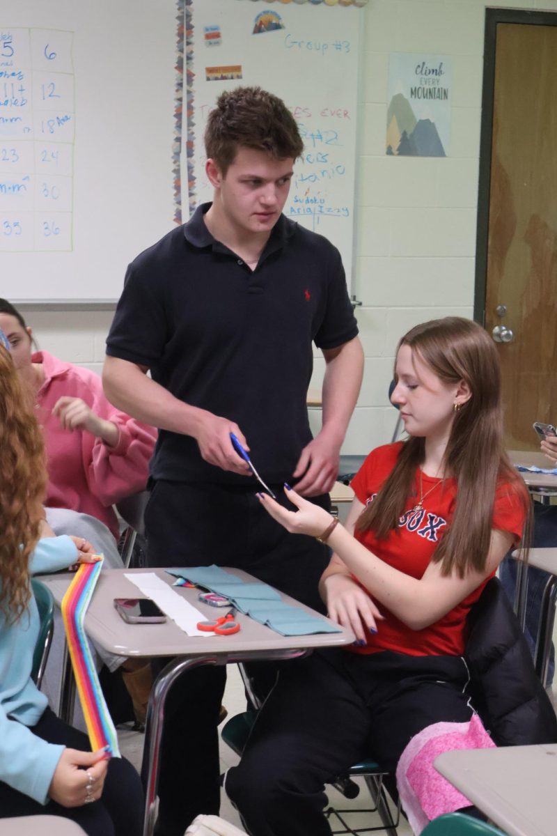 Talking with a peer, junior Spencer Phipps asks for scissors to make a scrunchie. On April 9 math teacher Renae Muzer hosted a sewing class during SRT.