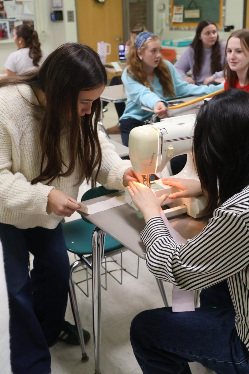 Assisting her classmate, Senior Isabel Bhagat, shows Alicia Verscheure how to sew. On April 9, teacher Renee Muzer hosts a sewing class during her SRT.