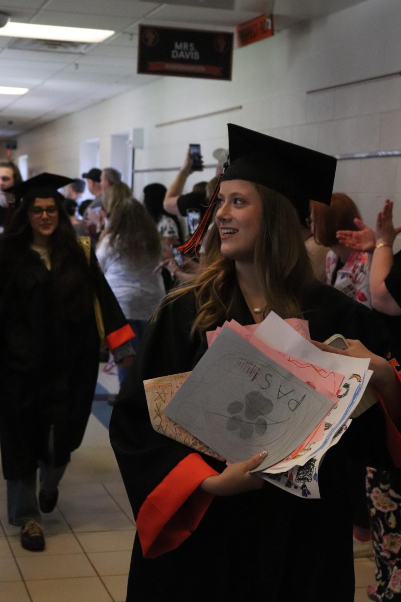 Holding her art pieces, Senior Violet Lewis shows off her artwork from elementary school that they still hold onto. On May 14, Senior had a clap out at Tomek.